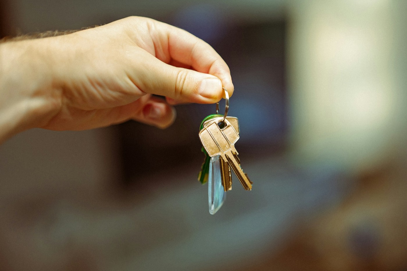 Close-up of a hand holding up a ring of house keys against a soft, blurred background
